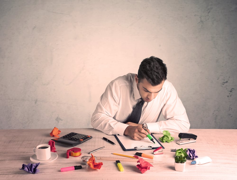 A young office worker sitting at desk working with keyboard, papers, highliter in front of empty clear background wall concept