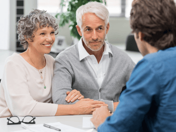 Picture showing a happy couple consulting with a mortgage broker with forms laid out on table